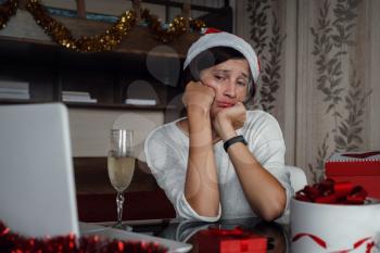 Concept of Christmas online shopping, buying gifts, congratulations over Internet. sad lady sits with laptop, looks at the screen. Nearby gift boxes. white and red