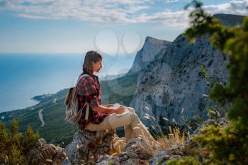 woman hiker enjoy the view at mountain peak cliff, writes notes, ideas in his paper notebook. idea of ecotourism travel. Discovery Travel Destination Concept