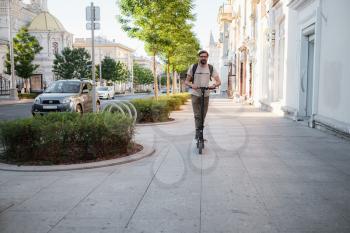 fun driving electric scooter through the city. A hipster man enjoys a walk through the city during the summer sunset. The idea and concept of ecology, style and fun moving around the city