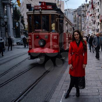 Fashion style portrait of young beautiful young woman posing at city street in Taksim, steet with red train. A girl walks through winter Istanbul.
