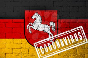 Flag of the regions of Germany Lower Saxony with original proportions. stamped of Coronavirus. brick wall texture. Corona virus concept. On the verge of a COVID-19 or 2019-nCoV Pandemic.