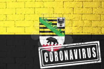 Flag of the regions of Germany Saxony-Anhalt with original proportions. stamped of Coronavirus. brick wall texture. Corona virus concept. On the verge of a COVID-19 or 2019-nCoV Pandemic.