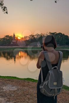 tourist girl taking pictures at sunset Sukhothai Historical Park, a UNESCO World Heritage Site in Thailand, beautiful flowering park and old chedi ruins, mobile photo
