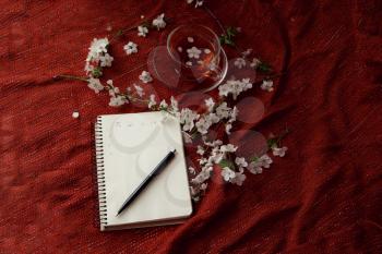 Spring flat lay top view home office workspace - notebook with tea cup and cherry blossom branches on a red desk background