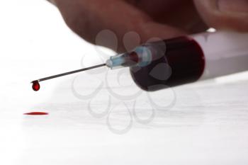 Macro view of drop of blood from syringe with male hand over white background. Blood chemistry. Blood test for viruses.
