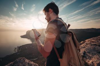 Man backpacker using smartphone relaxing on mountain top traveling alone. lifestyle active vacations modern technology millennials concept. Marvelous daybreak.