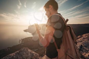 Man backpacker using smartphone relaxing on mountain top traveling alone. lifestyle active vacations modern technology millennials concept. Marvelous daybreak. mock up text.