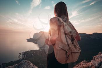 Young woman in a sports dress with backpack enjoys the view of the mountains and the sea at sunset. Travel and active lifestyle concept. Glamping