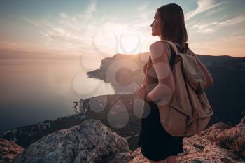 Young woman in a sports dress with backpack enjoys the view of the mountains and the sea at sunset. Travel and active lifestyle concept. Glamping
