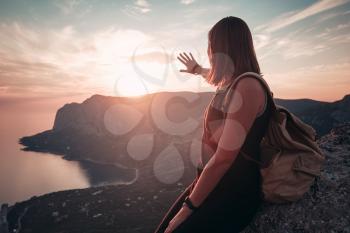 Young woman with a backpack enjoys the view of the mountains and the sea at sunset. Lifestyle emotional concept vacations weekend getaway aerial Crimea landscape