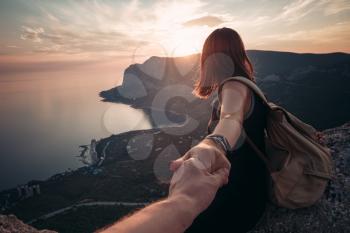 Girl standing on the mountain top over blue sea view. Follow me - POV. Couple enjoying a hike in nature. The concept of the journey to the meeting of new discoveries