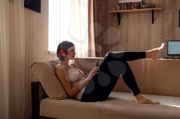 Young woman isolating at home and relaxing: stay at home social media campaign for coronavirus prevention. chatting with friends and using apps on a smartphone