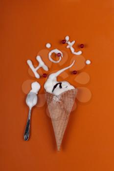 Ice cream cone filled with vanilla ice cream on an orange background. Summer concept. and the inscription Hot written by melted ice cream