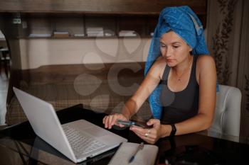 Shot of pretty young woman using her mobile phone while working with laptop sitting at home. Working from home in quarantine lockdown. Social distancing Self Isolation