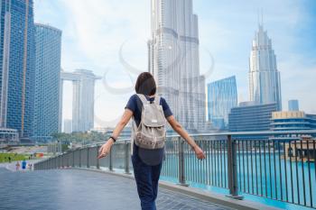 Young beautiful woman enjoying the view of Dubai downtown. Enjoying travel in United Arabian Emirates. view from the back or rear view, the lady walks away from the photo camera