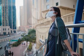 Happy young female traveler with white protective mask in the big city of Dubai, famous place Dubai marina. Luxury and comfortable tourism season in United Arab Emirates. The New Reality and the Norm