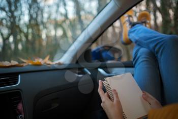 Modern hipster woman resting in a car and reading. . Feet outside the window at sunset forest. The concept of freedom of movement. An autumn weekend in nature.
