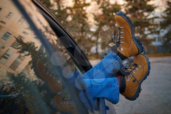 Woman feet in trendy yellow hiking boots on car door. Feet outside the window at sunset forest. The concept of freedom of movement. An autumn weekend in nature.