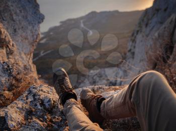 Close Up view on male feet wearing hiking boots. Man tourist sitting on the edge cliff mountains above sea