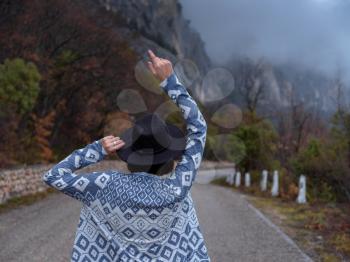 Back view of Stylish hipster woman in hat and poncho walking down a mountain road. The concept of travel and wanderlust. An amazing atmospheric moment