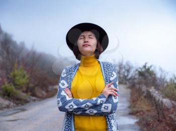 Stylish hipster woman in hat and poncho walking down a mountain road. The concept of travel and wanderlust. An amazing atmospheric moment