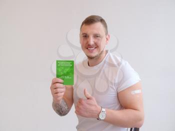 Adult man wearing t-shirt holding green International Certificate of Vaccination on white background. Traveling Immune passport, as proof vaccinated against Covid-19.