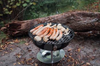 row of pork and beef bratwurst grilling over a barbecue fire on the summer vacation. Grilled sausage with mushroom on the picnic flaming grill