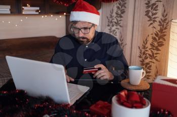 Happy man wearing Santa Claus hat . Buying christmas gifts online - online shopping concept. Ecommerce website xmas time holiday online shopping sale.