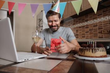 Man celebrating birthday online in quarantine time. Coronavirus outbreak 2020. The guy opens the box and is very happy with the gift. Communicating with friends remotely