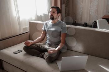 millennial hipster guy enjoy no stress peace of mind lounge on sofa at home. Men do meditation with laptop and phone on sofa