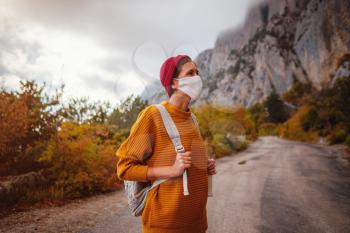 A young woman with a protective face mask is on a walk in nature and she is thinking about when the quarantine ends - topic of corona virus - COVID 19. Wanderlust photo series.