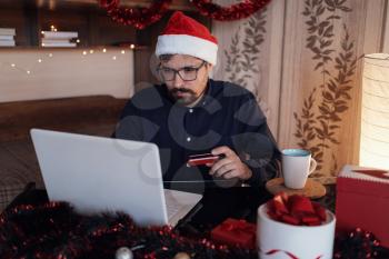 Happy man wearing Santa Claus hat . Buying christmas gifts online - online shopping concept. Ecommerce website xmas time holiday online shopping sale.