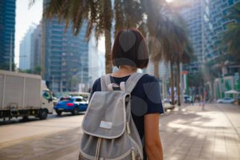 Portrait of young woman wearing in blue dress and white mask for prevent virus, walk in front of skycrapers in modern city. view from the back or rear view, the lady walks away from the photo camera