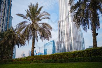 DUBAI, UNITED ARAB EMIRATES - FEBRUARY 10, 2021: Bottom-up view of Burj Khalifa in contrast with the blue sky and clouds. At the bottom of the building, there is some green palms.