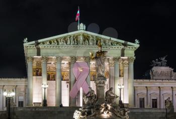 Illuminated facade of Austrian Parliament building with pink cancer ribbon in Vienna, Austria