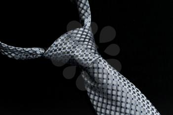 Detail of a windsor knot on gray and blue knotted tie isolated against black background