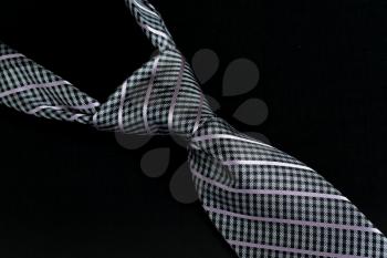 Detail of a windsor knot on gray and blue knotted tie isolated against black background