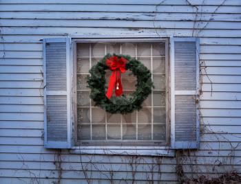 Traditional design of a christmas wreath attached to the window of an old and delapidated home with peeling paintwork