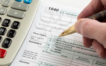 Male caucasian hand holding pen above USA tax form 1040 for year 2014  and calculator illustrating completion of tax forms for the IRS