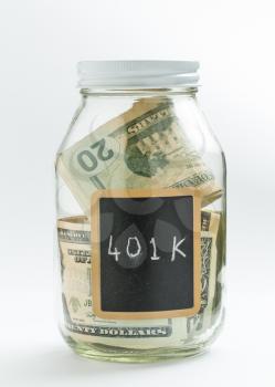 Glass jar on white background with black chalk label or panel and used for saving of US dollar bills for 401K retirement savings and fund