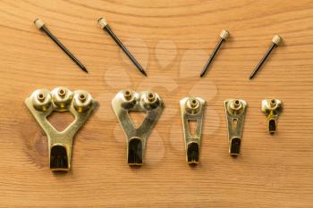 Set of five different sized brass picture hooks and nails or pins against a wood background