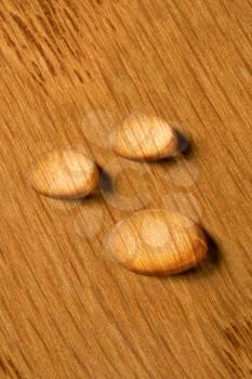 Three round water drops standing on polished wood surface of flooring or other hardwood