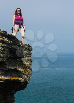Female hiker stands on cliff edge near the South West Coast Path at Tintagel, Cornwall, England, UK