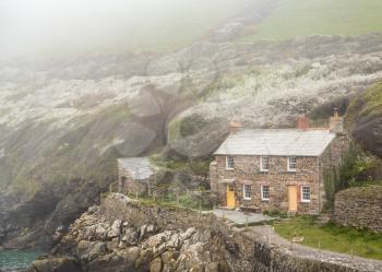 View of stone cottage and hillside as the mists roll in over the ocean in Port Quin, Cornwall, England, UK