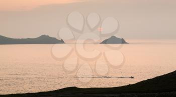Small boat races back to port by headland overlooking the coast at sunset at Port Quin, Cornwall, England, United Kingdom