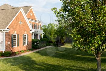Front of home and garage of large single family modern US house with landscaped gardens and lawn on a warm sunny summers day