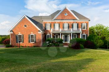Front of home and garage of large single family modern US house with landscaped gardens and lawn on a warm sunny summers day