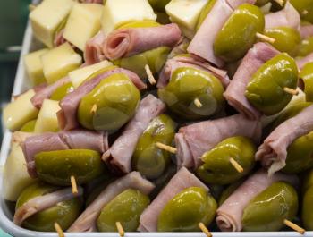 Green olives, ham and cheese on plate of hors-d'oeuvres or entradas in food counter in Spanish market in Madrid