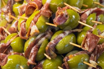 Green olives and Iberian ham or bacon on plate of hors-d'oeuvres or entradas in food counter in Spanish market in Madrid