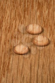 Three round water drops standing on polished wood surface of flooring or other hardwood